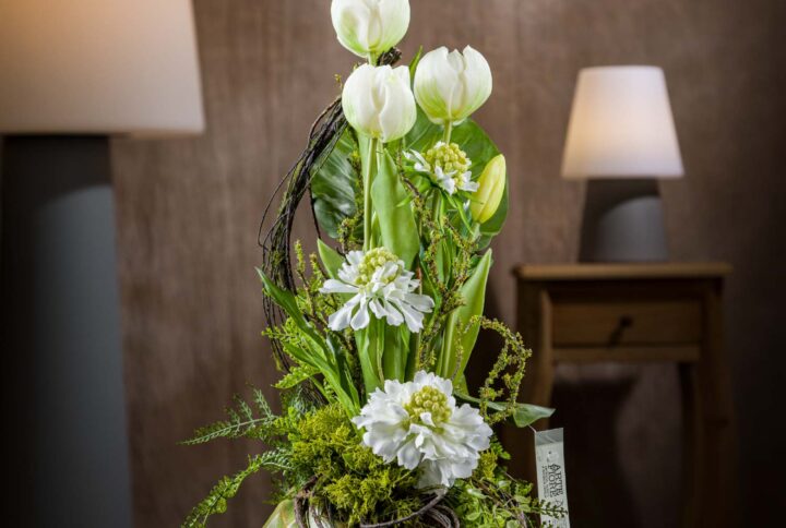 Vista frontale della composizione di tulipani finti, un elegante complemento d'arredo con fiori artificiali di alta qualità, disposti in un raffinato vaso di ceramica verde di design.