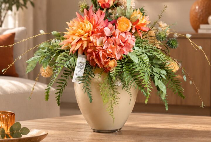 Primo piano del grande fiore dai petali arancio e corallo, con rose bicolori e infiorescenze sferiche verdi e crema.