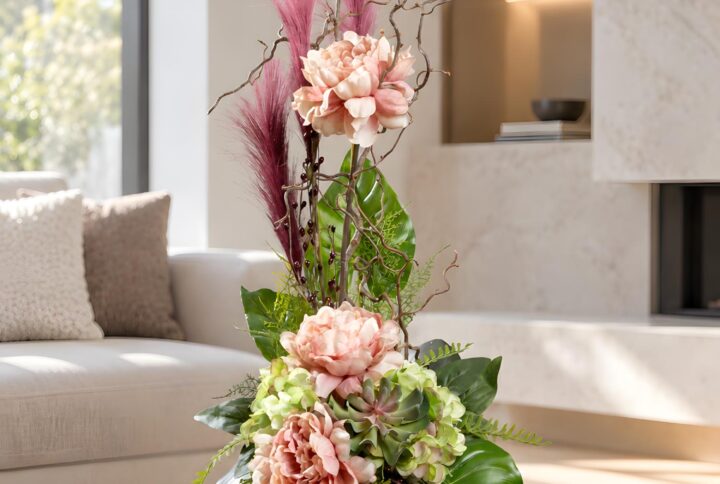 Composizione floreale artificiale rosa in vaso di ceramica, con peonie, ortensie verdi e rami slanciati, ambientata davanti al camino.