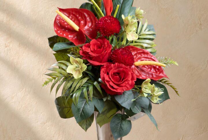 Fiori finti che sembrano veri nel mazzo per loculo con Anthurium e rose rosse, fogliame verde ed elementi slanciati, vista frontale.