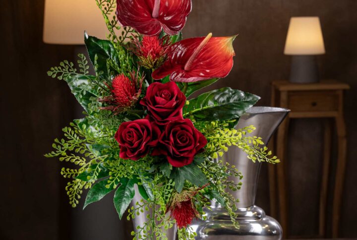 Vista frontale del mazzo di fiori finti che sembrano veri, composto da Anthurium rossi e rose rosse in un elegante vaso argentato