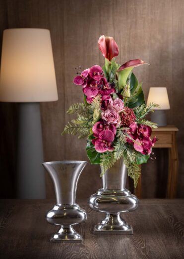 Vista frontale di una composizione floreale con orchidee finte per cimitero, caratterizzata da tonalità intense e profonde di rosa e fucsia, collocate in un vaso elegante.