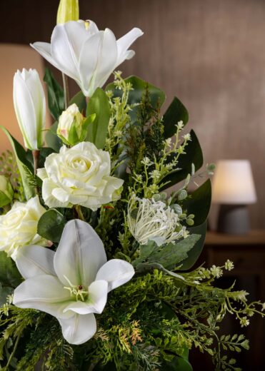 Dettaglio di gigli artificiali bianchi e foglie verdi in composizione funebre – Fiori per cimitero che durano