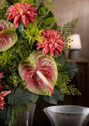 Ritaglio ravvicinato di una composizione floreale invernale per cimitero con dalie rosse e foglie – calore e colore per un omaggio invernale duraturo