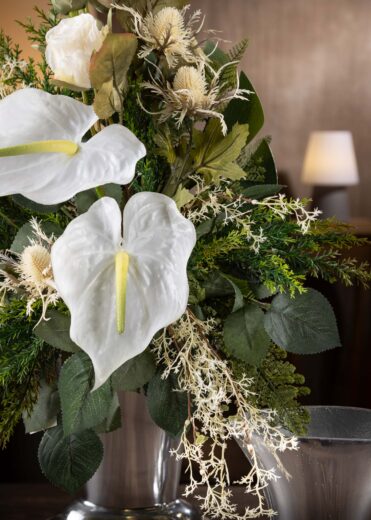 Dettaglio ravvicinato di un mazzo di fiori artificiali finti per cimitero e loculo - mostra anthurium bianchi e dettagli di piante verdi, con un aspetto realistico e resistente