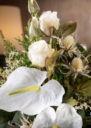 Dettaglio delle foglie di un mazzo di fiori artificiali finti per cimitero e loculo - la cura artigianale nella disposizione delle foglie e dei fiori bianchi crea un effetto elegante e armonioso