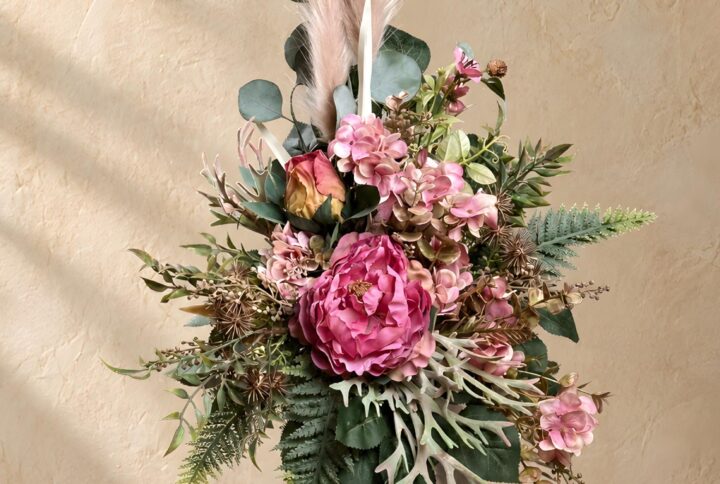 Mazzi di fiori per cimitero nei toni del rosa con Ortensie, fogliame grigio-verde e piume decorative chiare, vista frontale.